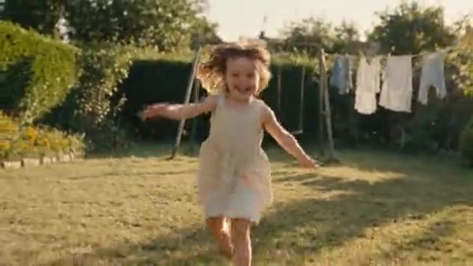 Imagen de un clip de vídeo de 480 × 270 píxeles: una niña pequeña corre hacia la cámara en un jardín soleado, con ropa tendida al fondo.