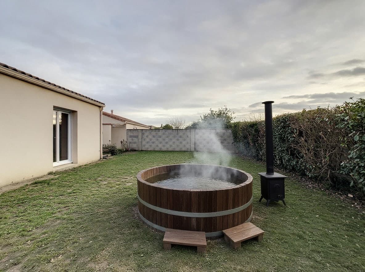 Derselbe Garten mit einem runden, dampfenden Badefass aus Holz mit Metallreifen und seinem kleinen schwarzen Ofen daneben