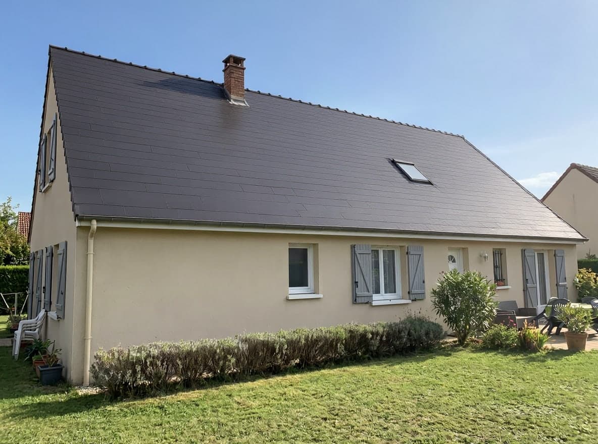 Dasselbe Haus mit einem Dach aus matten anthrazitfarbenen Flachziegeln, unter einem einheitlich blau gewordenen Himmel