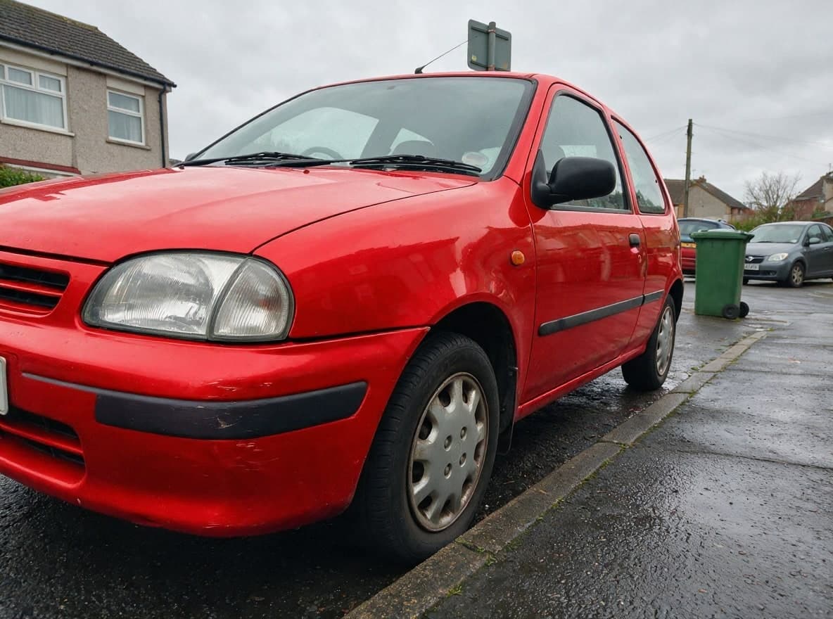 Dasselbe Auto in leuchtendem Metallic-Rot, Radkappen und Kratzer unverändert